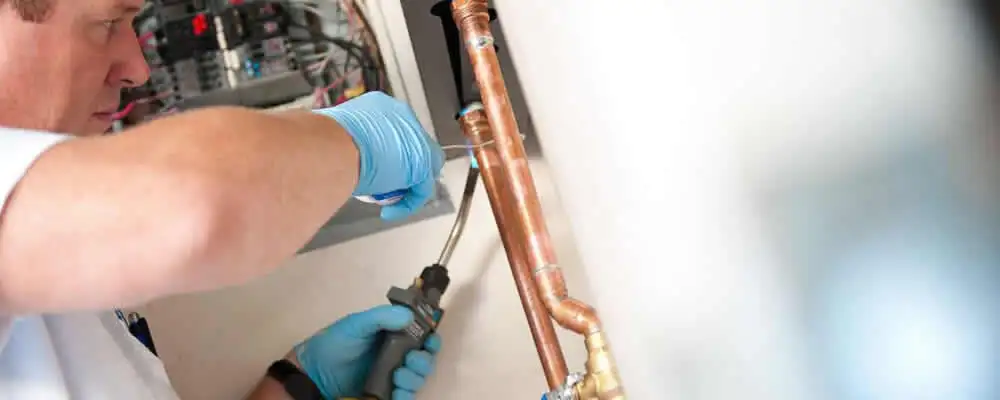 Water heater repair technician testing copper pipe connections and controls in Spokane, WA